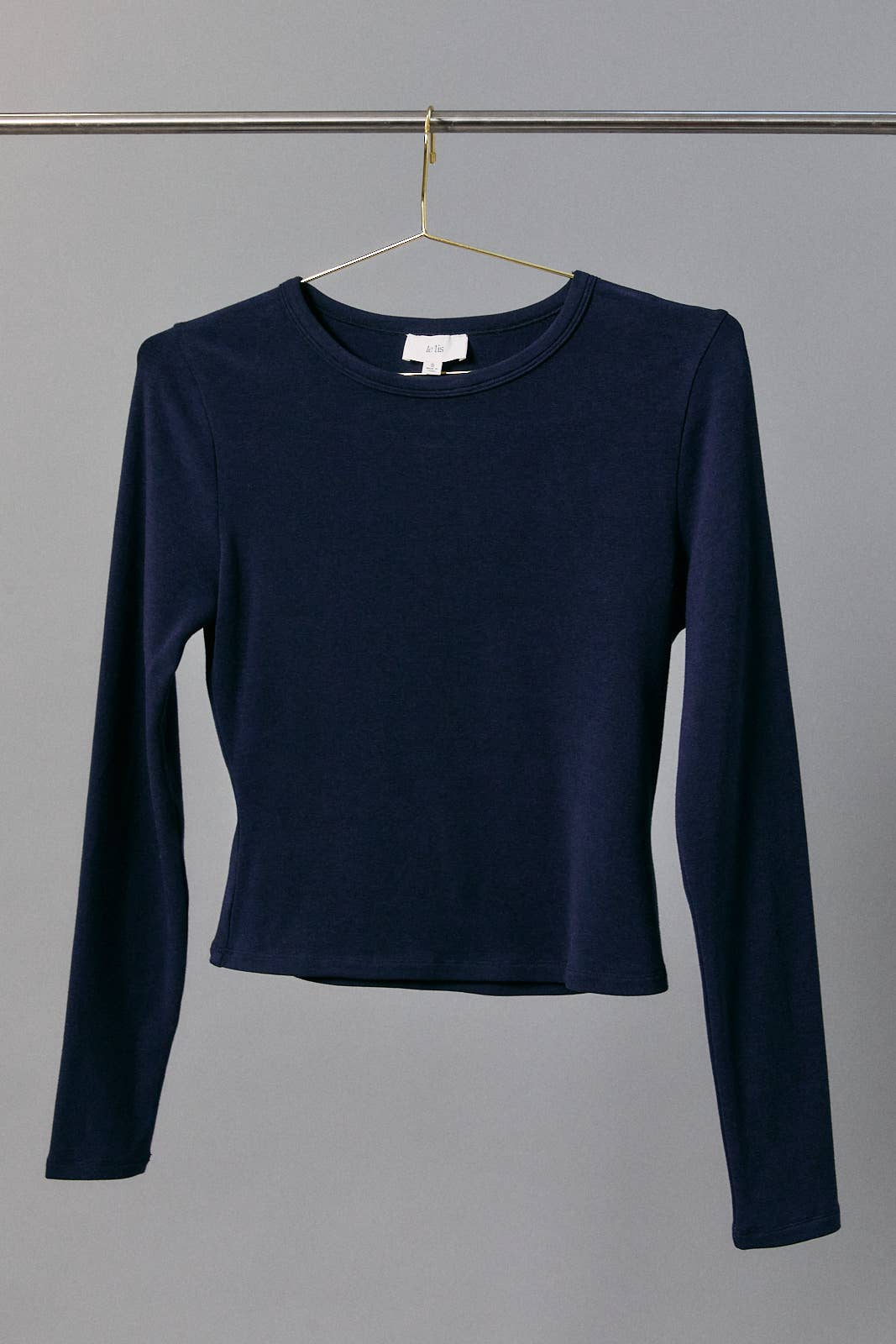 A navy blue long-sleeve crop top hanging on a gold hanger against a solid gray background.
