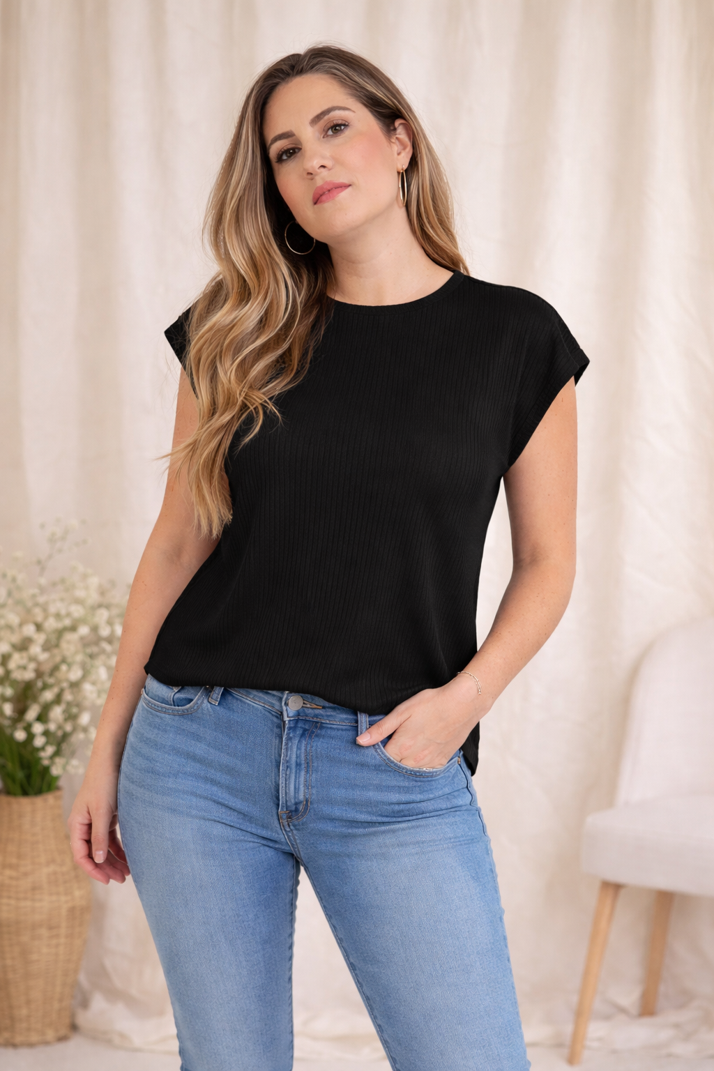 Woman wearing a black t-shirt and blue jeans against a neutral background