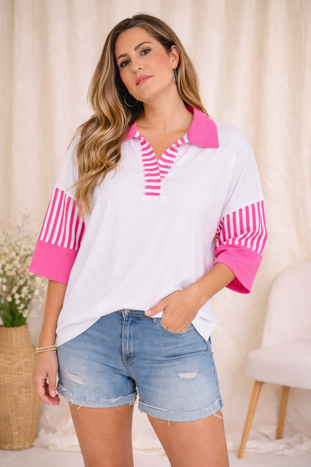 Woman wearing a white shirt with pink accents and denim shorts in a casual setting.