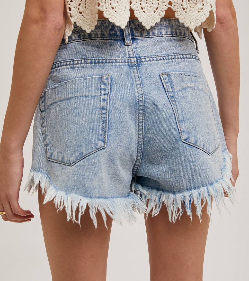 Denim shorts with frayed edges worn by a person on a plain background