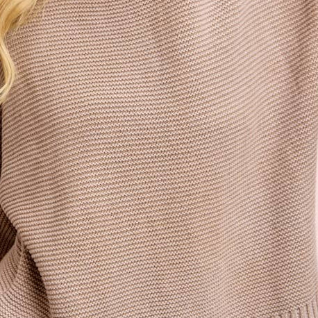 Woman wearing a beige sweater and blue jeans against a pink background