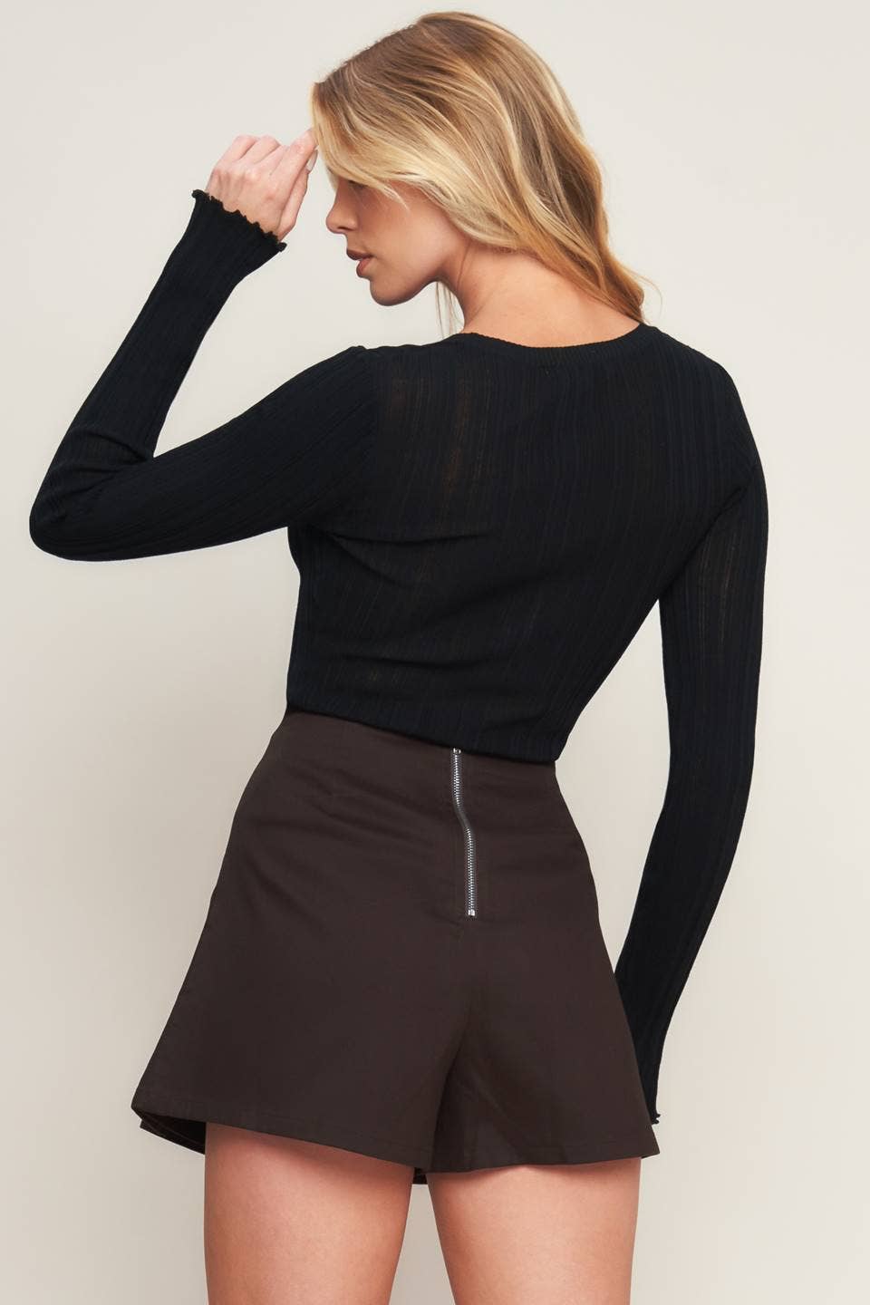 Woman wearing a black long-sleeve top and brown shorts on a plain background