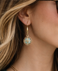 Close-up of a woman wearing a gold earring with a blue gemstone.
