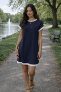 Woman in a navy dress walking along a path by a pond with trees and a bench in the background.