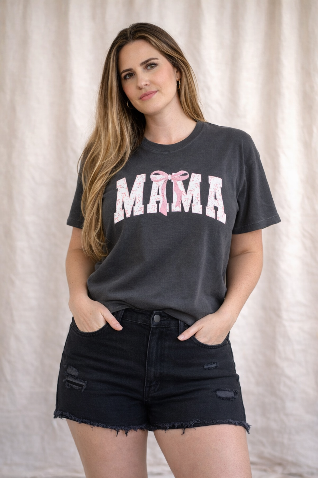 Woman wearing a black t-shirt with 'MAMA' and pink bows on a beige background