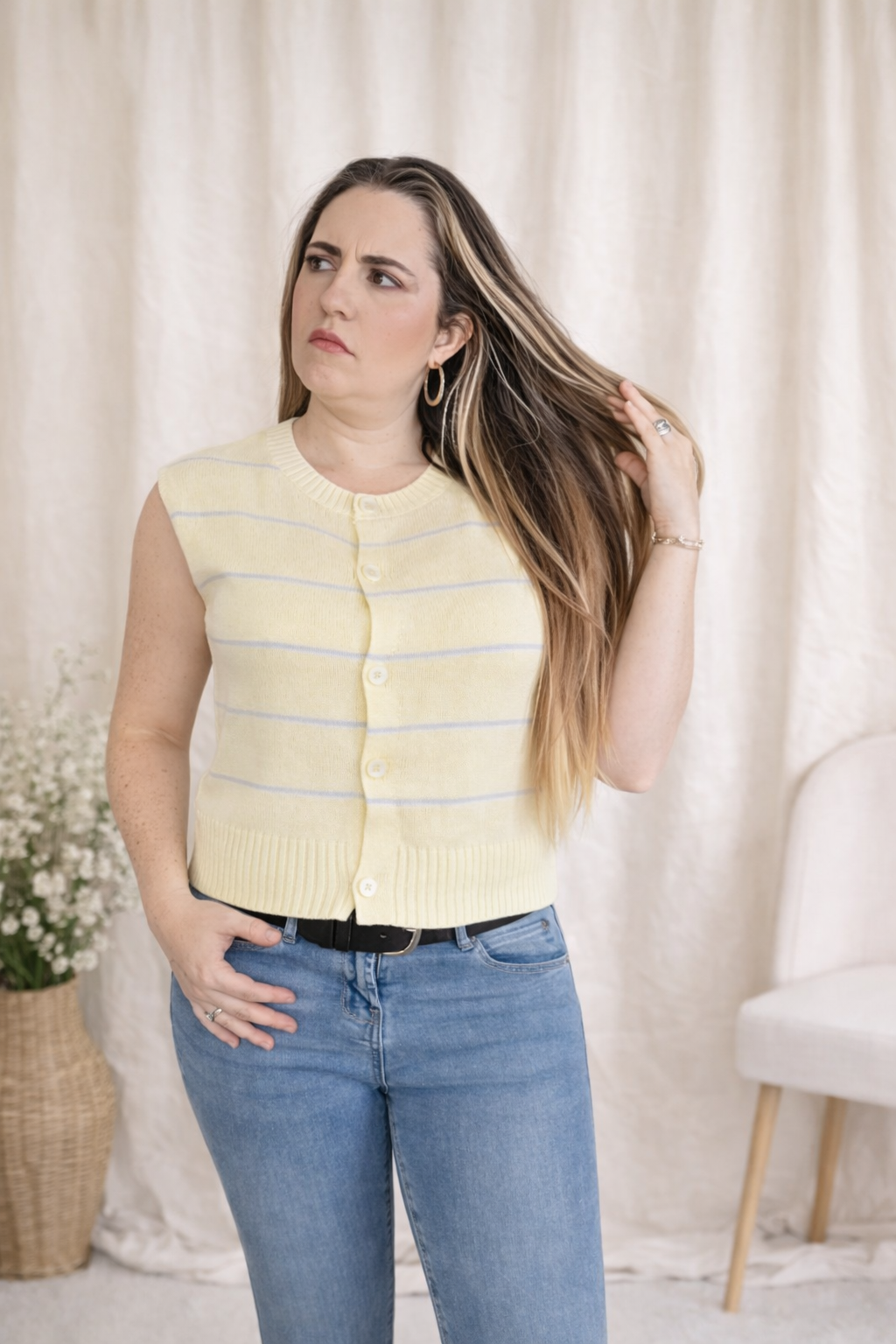 Woman wearing a yellow striped vest and blue jeans against a white curtain background