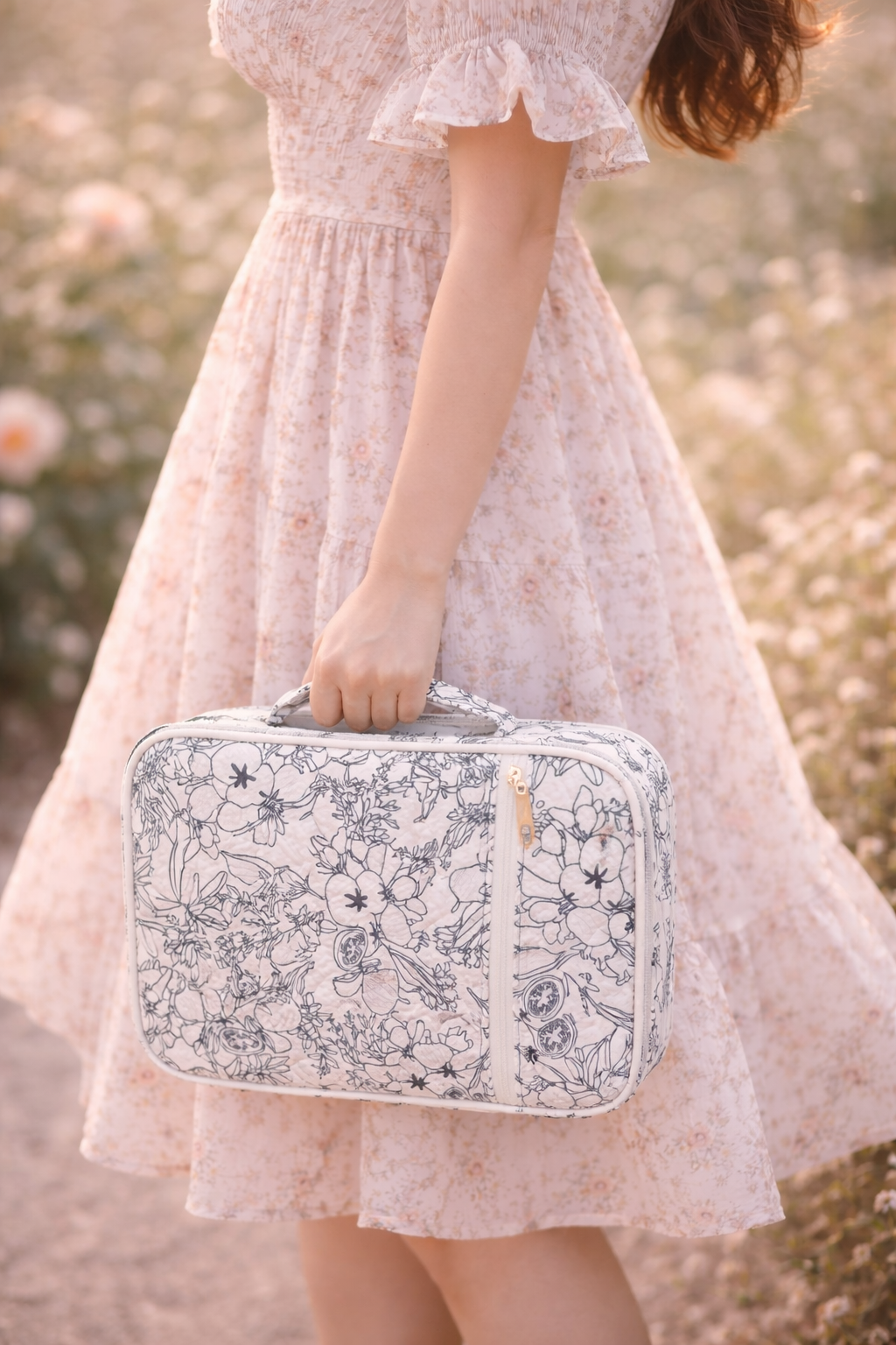 Person holding a floral-patterned suitcase in a field